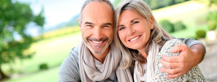 Pareja adulta sonriendo con confianza tras cuidar su salud bucodental